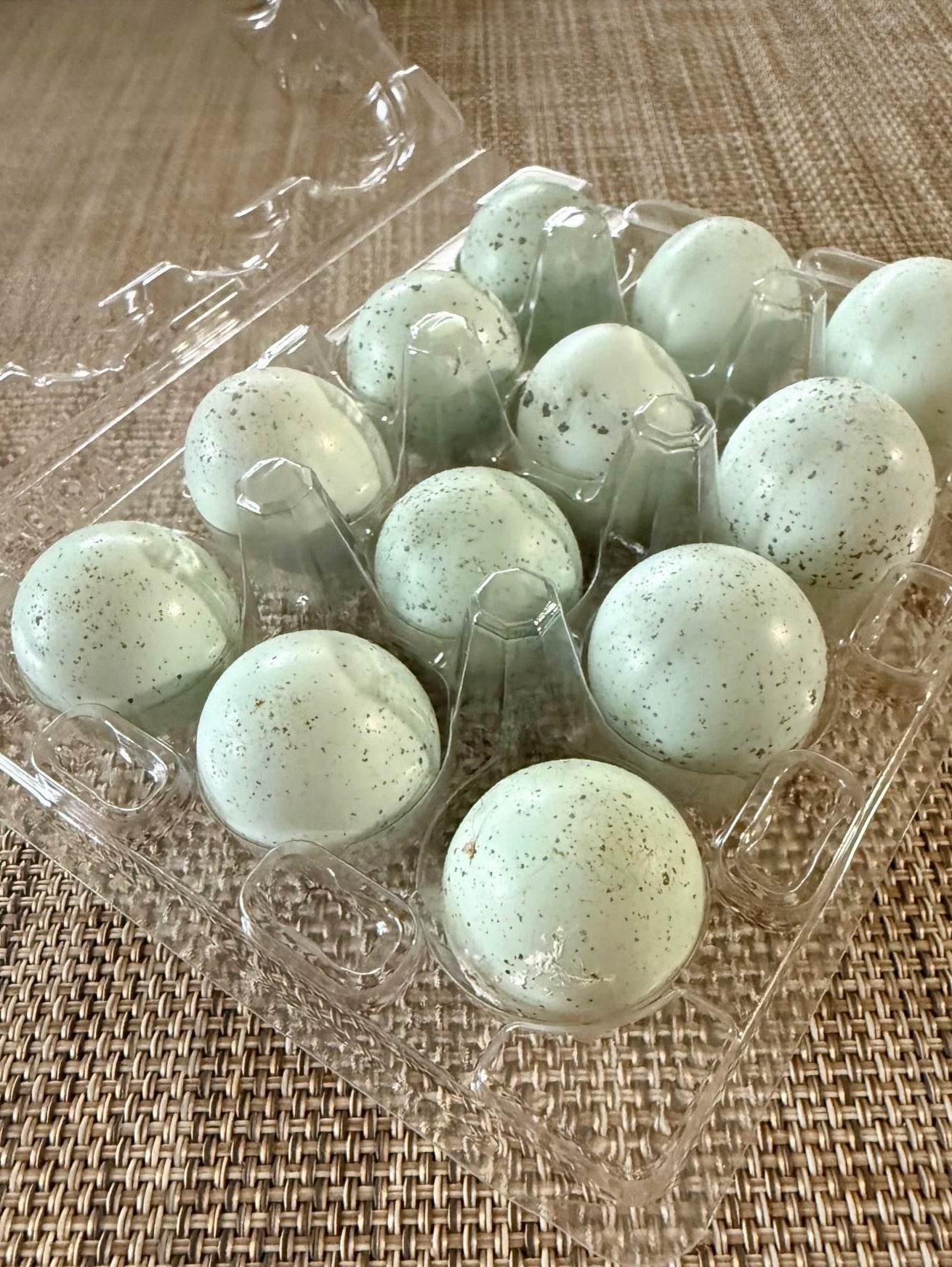 Carton of 18 light blue quail eggs in clear plastic packaging on a woven surface