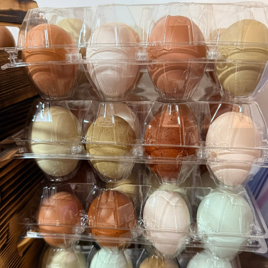 Assorted colored eggs in a clear plastic egg carton on a wooden surface.
